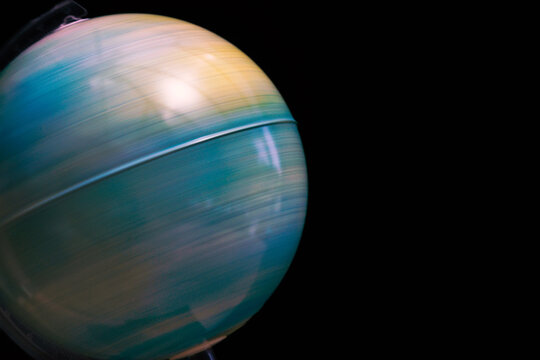 Slow shutter speed image of a world globe spinning creating a blurred effect. Globe set against a dark black board background. Concept image with copy space available.