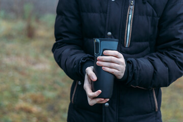 In late autumn, men's hands are warming themselves on a black toggle switch with a hot drink. Environmentally friendly use of reusable glasses, mugs. Rejection of plastic