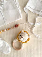 A baby's white suit, a hat for a newborn, scratches, socks, a rattle with a lion and a chain of wooden beads for teeth are lying on the bed. vertical photo