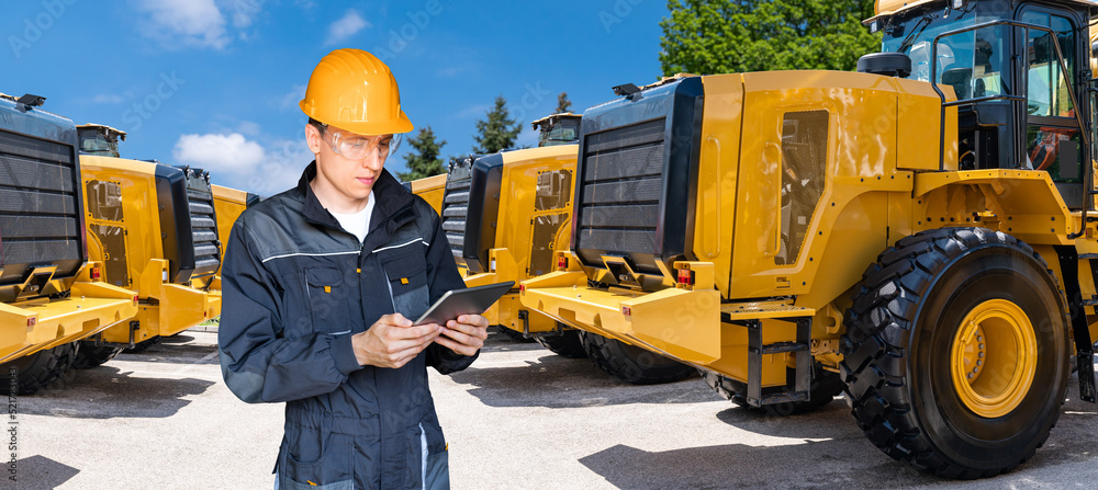 Poster engineer in a helmet with a digital tablet on the background of construction machines