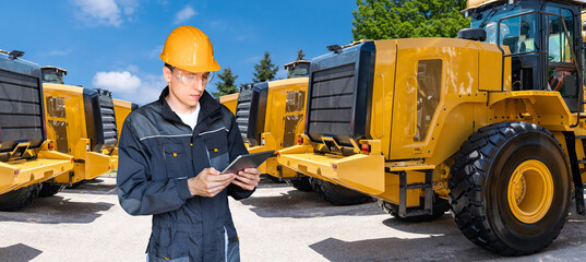 Engineer in a helmet with a digital tablet on the background of construction machines