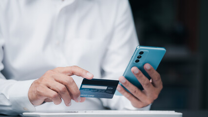 Young businessman using credit card to make financial transactions via smartphone, payment concept with wireless communication technology, focus on consumer safety and cashlessness.
