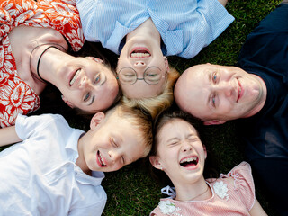 A happy family lies on the lawn with their heads to each other, look up and laugh. top camera