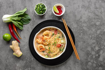 Laksa Shrimp bowl. glass noodle dish, top view, copy space. Asian Malaysian food with shrimps, bok choy, lime, ginger, and chili. Most variations of laksa are prepared with spicy coconut soup.