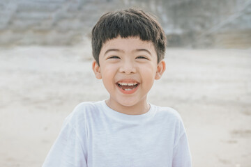 Portrait cute boy playing in the sandy beach, happy and Smiling and fun child. he wears a white shirt.