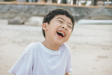 Portrait cute boy playing in the sandy beach, happy and Smiling and fun child. he wears a white shirt. © suvita style 