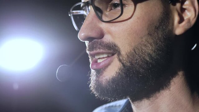 Portrait of a young male business coach speaking through a microphone in a dark conference room. Profile of a young man speaking passionately from the stage