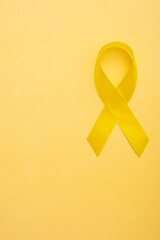 Childhood cancer awareness ribbon on yellow background. Copy space. Vertical format