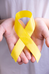 Childhood cancer awareness month symbol with yellow ribbon in child hands. Vertical format