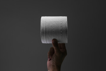 One hand holding a roll of toilet paper with spotlight effect and isolated dark grey background
