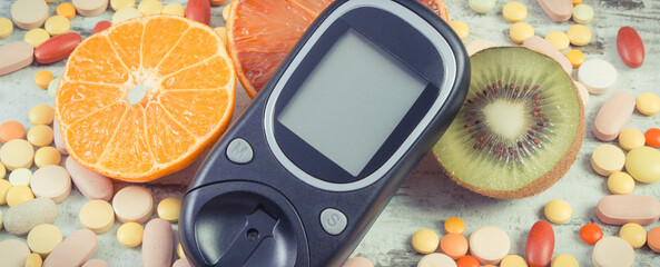 Glucometer for checking sugar level, fresh fruits and medical pills. Choice between eating fruits...