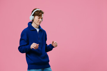 cute, joyful guy, happily dancing while standing in white headphones on a pink background. studio photographer on an empty background with space for an advertising layout
