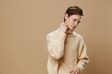 Obraz premium a man in a beige sweater poses standing sideways with his hand on his neck