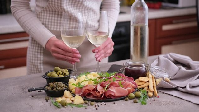 woman putting two glasses of wine to table with meat and cheese plater at domestic kitchen