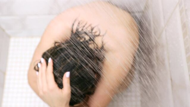 A naked, frustrated young woman squats in a corner in a shower under jets of water. A slim woman tries to cope with depression by taking a hot shower