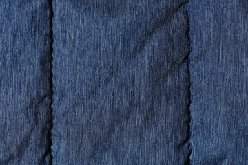 Fragment of blue fabric from a down jacket with seams. Texture, background for design.