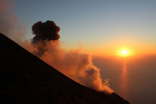 Sunset over the Stromboli volcano in Italy. Volcanic eruption, clouds of smoke in front of the ocean. Lava and gas explosion. Aeolian islands in the mediterranean sea.