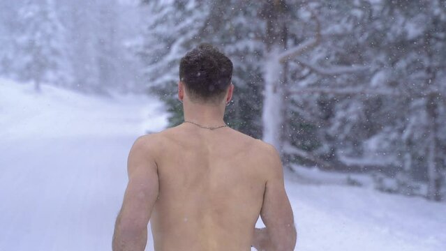 Running on snow in the forest in winter.
Naked man doing morning jog on snow. Masses of snow falling from pine trees in snowy weather.
