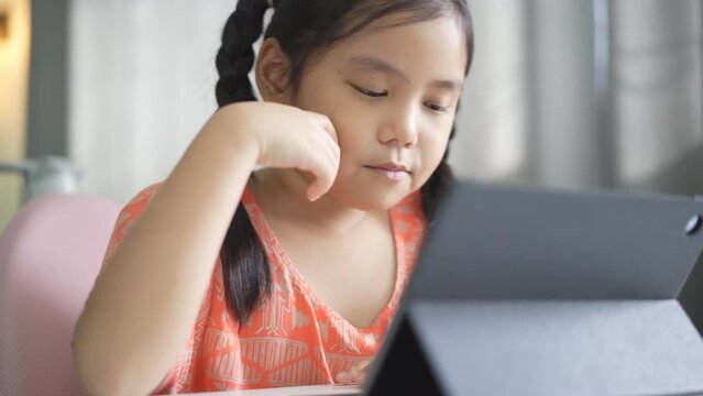 closeup asian child student enjoy studying online class on computer tablet or kid girl video call learning and smiling talking with suck candy taffy or person learn from home school in classroom