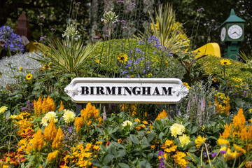 Birmingham city sign surrounded by flowers in garden of city centre park. Old black text on white...