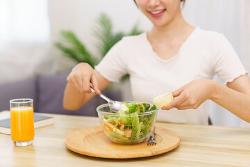 Lifestyle in living room concept, Asian woman using spoon to ladle salad dressing into salad bowl