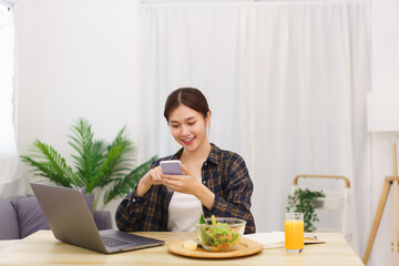 Obraz na płótnie Canvas Lifestyle in living room concept, Young Asian woman using smartphone and eating vegetable salad