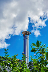 View to a stainless steel chimney in front of blue sky with clouds.