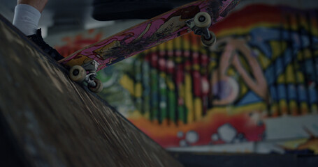 Sporty skater start riding on skateboard in ramp at skate park with graffiti. 