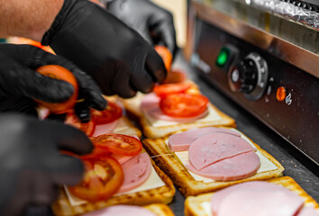 chef hand cooking sandwich with ham, cheese and vegetables on kitchen