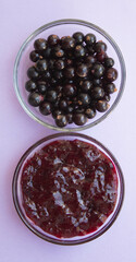 Berries fresh black currant and homemade jam in bowl. Violet background. Summer menu, natural vitamins. Top view.