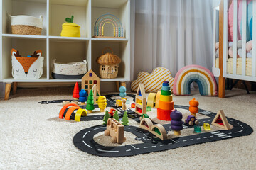 Fototapeta premium A toy town built in a children's room. Car track, toy cars, trees and wooden blocks for children's games in playroom. Educational game for baby and toddler in modern nursery.