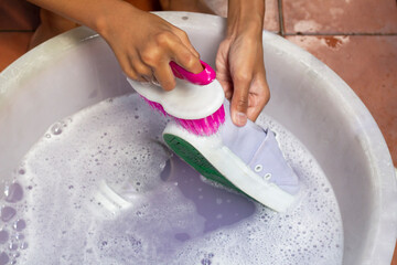 Hand of child holding a plastic brush washing the dirty shoes or sneakers in bubble-filled basin.