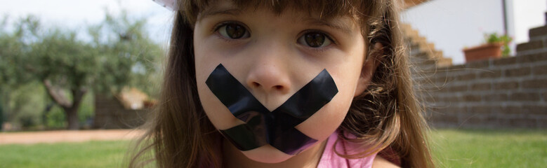 Image of an adorable little girl with a sad expression who has her mouth taped shut. Horizontal...