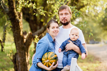 Fototapeta premium Portrait of Happy family hugging and spending time together outside in green nature. Young mother and father with little baby in garden. Apple harvest and picking on farm in autumn.