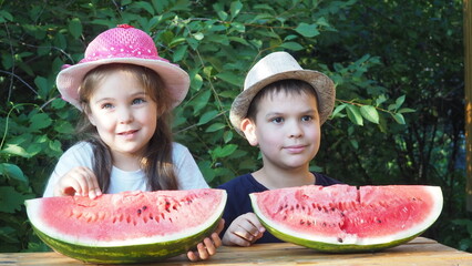 Cute baby girl 3-4 year old and boy eating tasty watermelon over green nature background close up. Healthy lifestyle. Childhood. Summer time. happy satisfied children smiling