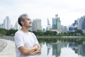 senior man with grey hair and beard standing and taking a deep breath after workout near the pond in nature atmosphere at the city park, concept for elderly people lifestyle,health care,well being