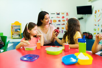 Preschool girl giving an apple gift to her happy teacher