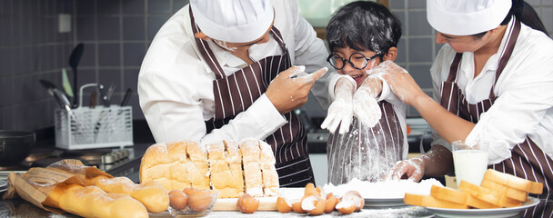 Cute asian boy with parent wearing chef hat apron preparing for baking dough in kitchen at home