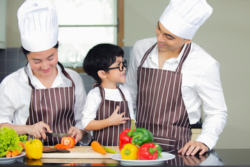 Happy  Asian  family  wearing chef hat.apron  cooking  salad in kitchen at home