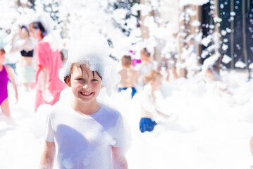 happy little boy with foam on his head, in wet clothes at a foam party or holiday on a sunny hot...