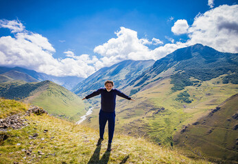 A man stands on top of a mountain with arms outstretched, North Ossetia, the village of Kamunta