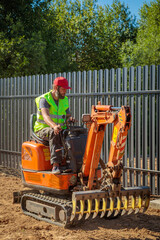 A man on a mini-excavator levels a piece of land, loosens the soil.