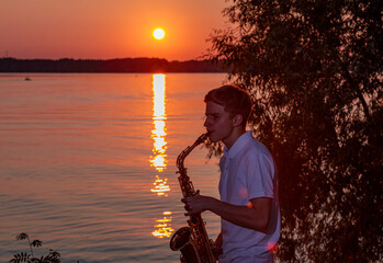 A young guy plays the saxophone in the evening at sunset