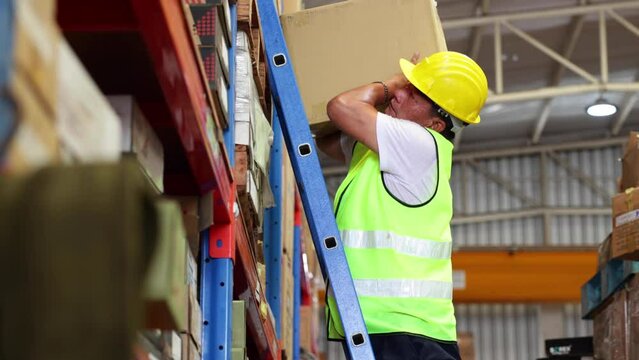 elderly male warehouse worker climbs the stairs to lift the cardboard boxes on the shelf. Yellow Safety hard hat helmet.