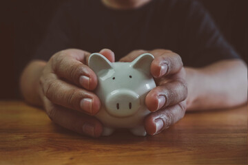 Man hand holding piggy bank on wood table. Save money and financial investment, Saving energy and...