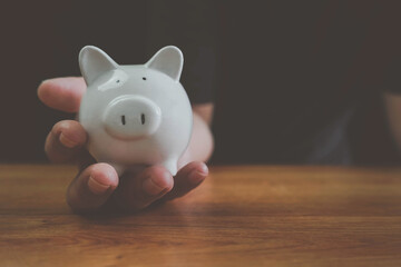Fototapeta na wymiar Man hand holding piggy bank on wood table. Save money and financial investment, Saving energy and money concept. idea for save or investment, The concept of saving money or savings, investment.