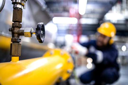 Close up view of natural gas pipeline with valve and refinery worker working in the background.