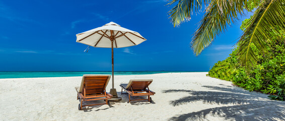 Beautiful tropical sunny shore, couple sun beds chairs umbrella under palm tree leaves. Sea sand...