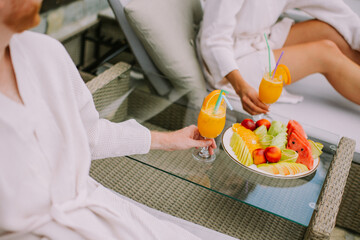 Young couple relaxing on beds and drinking fresh orange juice on the outdoor terrace