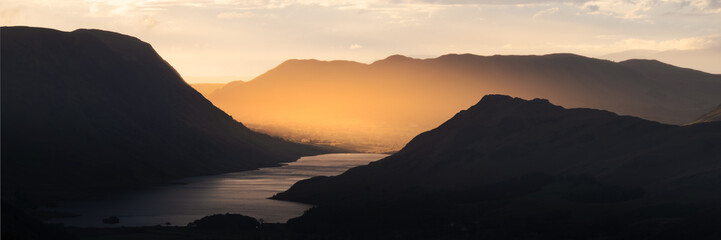 Beautiful golden light shining through shadow covered mountains. Crummock Water, Lake District, UK.